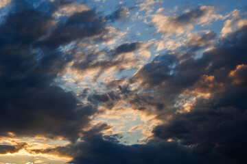 Naklejka na ściany i meble visuale in primo piano di un cielo azzurro, al tramonto, parzialmente nuvoloso, con nuvole color grigio e blu scuro, illuminato lateralmente dalla luce arancione del sole