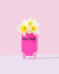Pink luggage with narcissus flowers and eyelashes. Surreal, minimal travel, adventure, tourism concept. Spring, summer season. Front view.