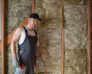 a construction worker insulates the wall of a frame house with insulation
