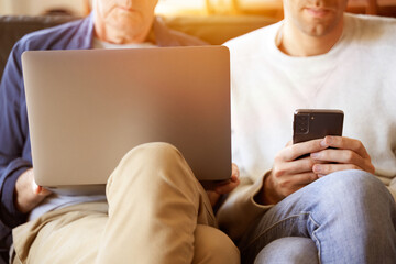 Father and son sitting using laptop and smartphone