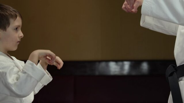 Little athlete performs blocks with his hands together with a trainer