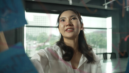 Professional businesswoman writing marketing idea on glass board. Smiling young beautiful project...