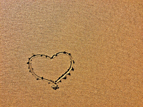 The image shows a heart shape drawn in the sand with fine grains.