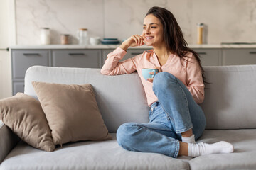 Cheerful woman enjoying cup of coffee on cozy sofa