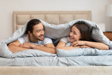 Cheerful couple enjoying cozy morning in bed, chatting and smiling - Powered by Adobe