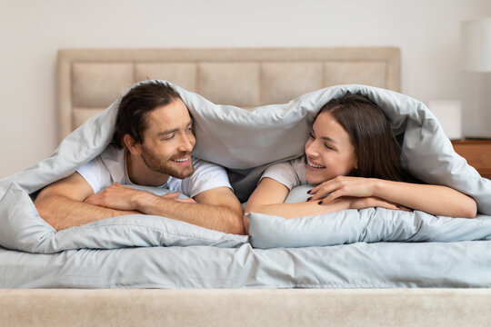 Cheerful couple enjoying cozy morning in bed, chatting and smiling