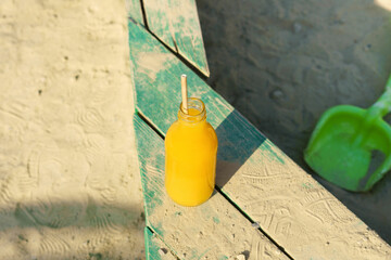 Orange or multivitamin mockup juice in a glass bottle in a children's sandbox. Thirst quenching concept, healthy drinks to go and snack during games