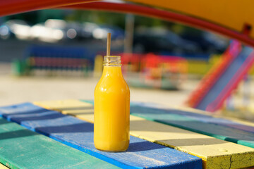 Close-up of natural orange juice mockup on the background of children's slides. The concept of baby food, summer drinks, thirst quenching - obrazy, fototapety, plakaty