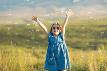 Funny little girl catching soap bubbles in the summer on nature. Cute child has happy fun with...