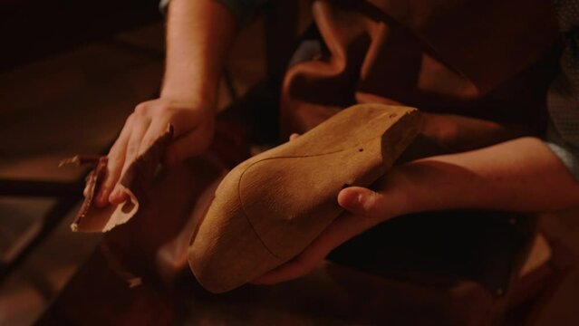 Shoemaker grinds wooden shoe last with sandpaper in workshop. Craftsman makes handmade shoes.