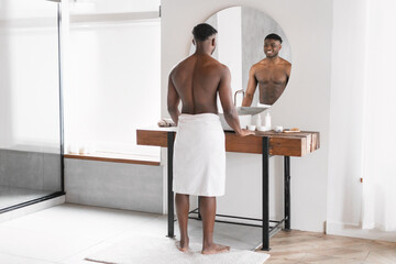 Back view African man shirtless stands near mirror in bathroom