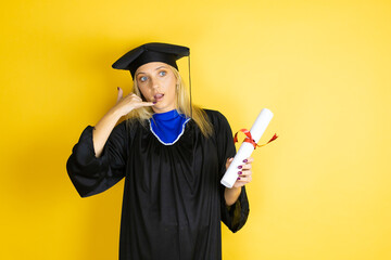 Beautiful blonde young woman wearing graduation cap and ceremony robe confused doing phone gesture...