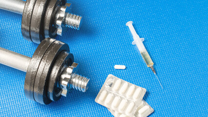 Doping in tablets and syringe on blue background next to dumbbells, concept of use of prohibited...