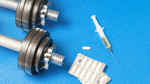 Doping in tablets and syringe on blue background next to dumbbells, concept of use of prohibited drugs in sports, oral and intramuscular medications.