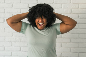Angry african american woman screaming on brick background. Bad aggressive emotions and premenstrual syndrome or pms concept