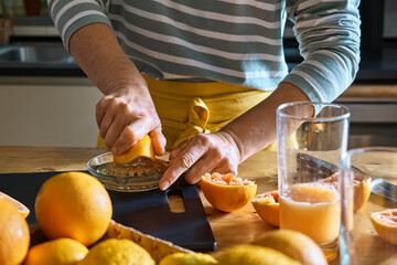 Female hands making homemade grapefruit juice with hand citrus juicer. Anonymous woman preparing...