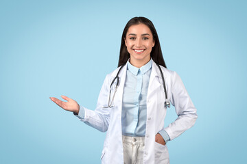 Smiling woman doctor presenting something with hand on blue backdrop