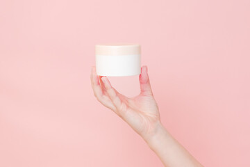 Hand holding jar of cosmetic cream on pink background. Cosmetics beauty mockup for product branding