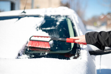 A young man wearing black warm suit for cleans his car after a snowfall on a sunny, frosty day.