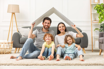 Family housing concept. Happy woman and her husband holding plastic roof while sitting with kids on floor at home