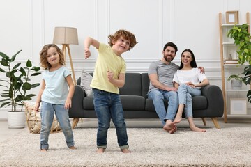 Happy children dancing while their parents looking at them in room