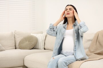 Fototapeta na wymiar Pregnant woman suffering from headache on sofa at home, space for text