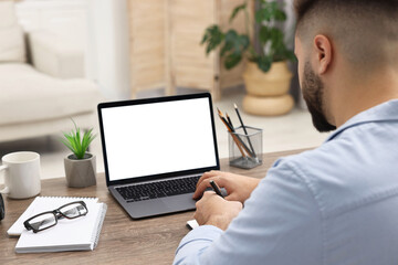 E-learning. Young man using laptop at wooden table indoors, closeup