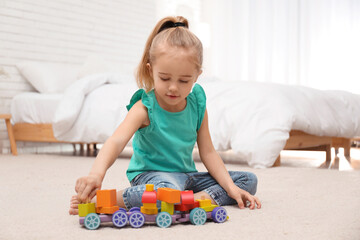 Cute child playing with wooden train on floor at home