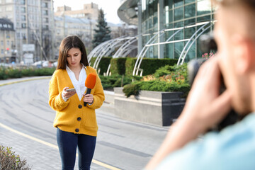 Young journalist and video operator working on city street