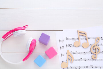 Notes, music sheets, headphones and cubes on white wooden table, flat lay with space for text. Baby...
