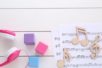 Notes, music sheets, headphones and cubes on white wooden table, flat lay with space for text. Baby...