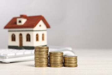 Mortgage concept. Stacks of coins, model house and calculator on white wooden table, selective focus with space for text