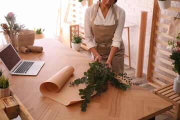 Florist making beautiful bouquet at table in workshop, closeup