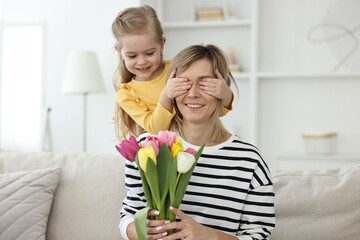 Fototapeta na wymiar Little girl surprising her mom with bouquet of tulips at home. Happy Mother`s Day