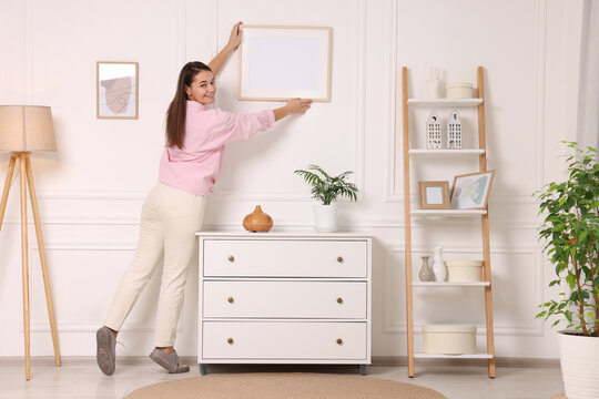 Woman hanging picture frame on white wall at home