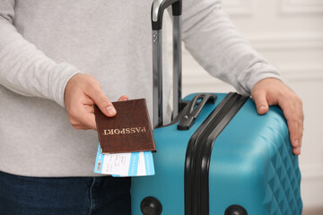Tourist with suitcase giving passport and tickets on blurred background, closeup