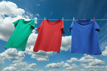 Colorful t-shirts drying on washing line against blue sky, low angle view
