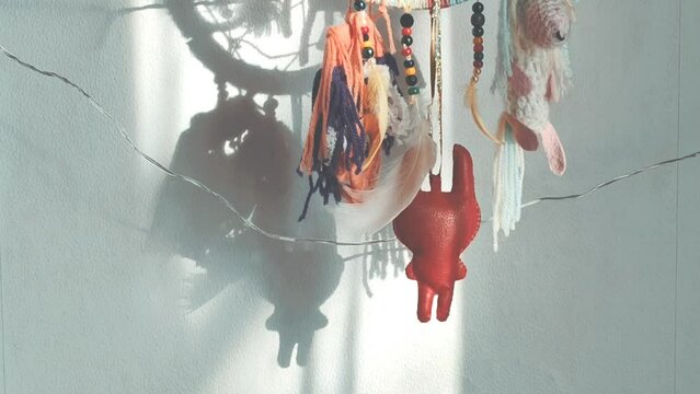 Handmade dream catcher with feathers and toys in sunlight hanging on the wall. 