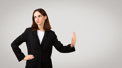 Distrustful businesswoman in a black suit jacket showing a stop hand sign