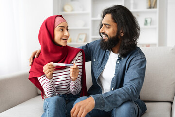 Happy Muslim Couple Holding Positive Pregnancy Test And Looking At Each Other