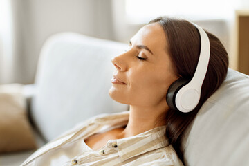 Peaceful young woman reclining on couch and listening music through her headphones