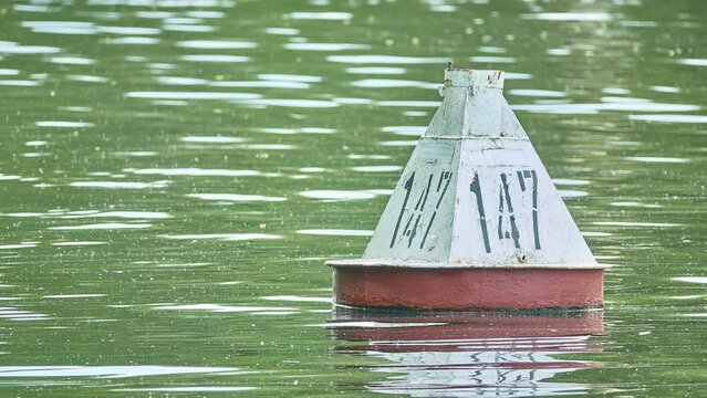 An old buoy with the number 147 floats on the surface of the water of a large lake.