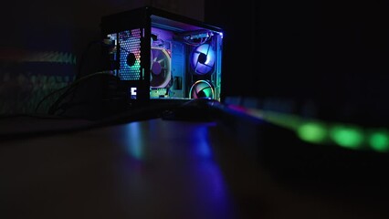 Desktop gaming PC in a dark room glowing with rainbow colors, camera focus shifts from the keyboard on the table to the background.