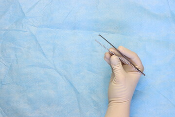 Surgical forceps in a surgeon hand wearing sterile gloves with a surgical surface with copy space...