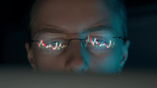 Trader wearing glasses is working on laptop computer. Screen with stock market charts and Bitcoin BTC or Ethereum ETH data analysis reflection. Broker trading online. Altcoins crypto currency trading