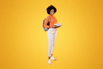 Confident young woman with a beautiful afro carrying a grey backpack and a stack of notebooks