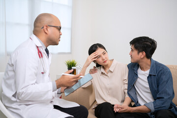 A dark tanned male doctor in a white medical suit discusses a woman's pregnancy. A male doctor opens an iPad showing pregnancy information and recommending dietary supplements and fertility care.