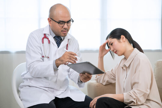 Foreign tanned male doctor in white medical clothes discussing woman's illness male doctor opens an iPad, shows treatment and medication information, and provides information of each drug.