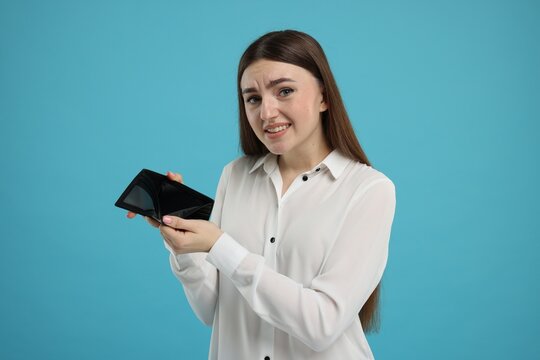 Woman showing empty wallet on light blue background