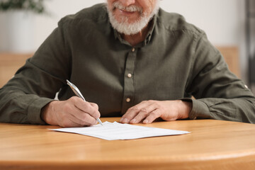Senior man signing Last Will and Testament at wooden table indoors, closeup